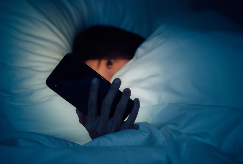 girl in bed looking at phone at night